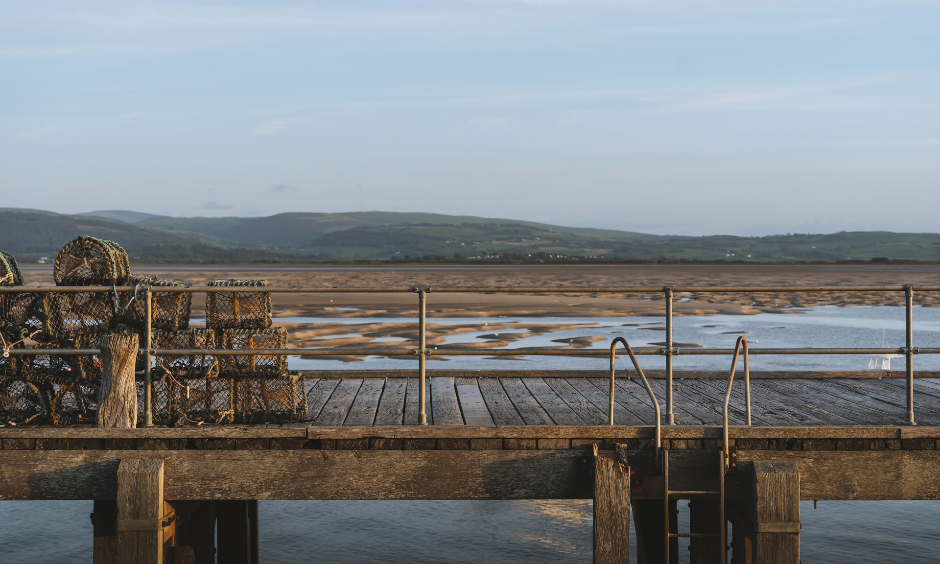 A jeti at Aberdyfi with lobster cages piled high and a sandy shore in the distance.