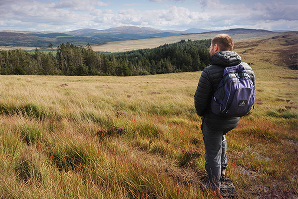 A man standing on grass, wearing a backpack looking into the distance at Bwlch Drws Ardudwy