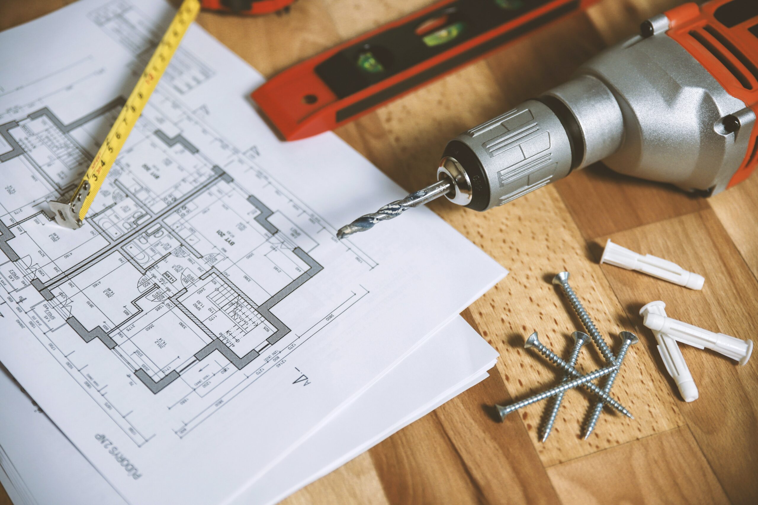 A drill, screws, level and planning drawings are strewn on a table.