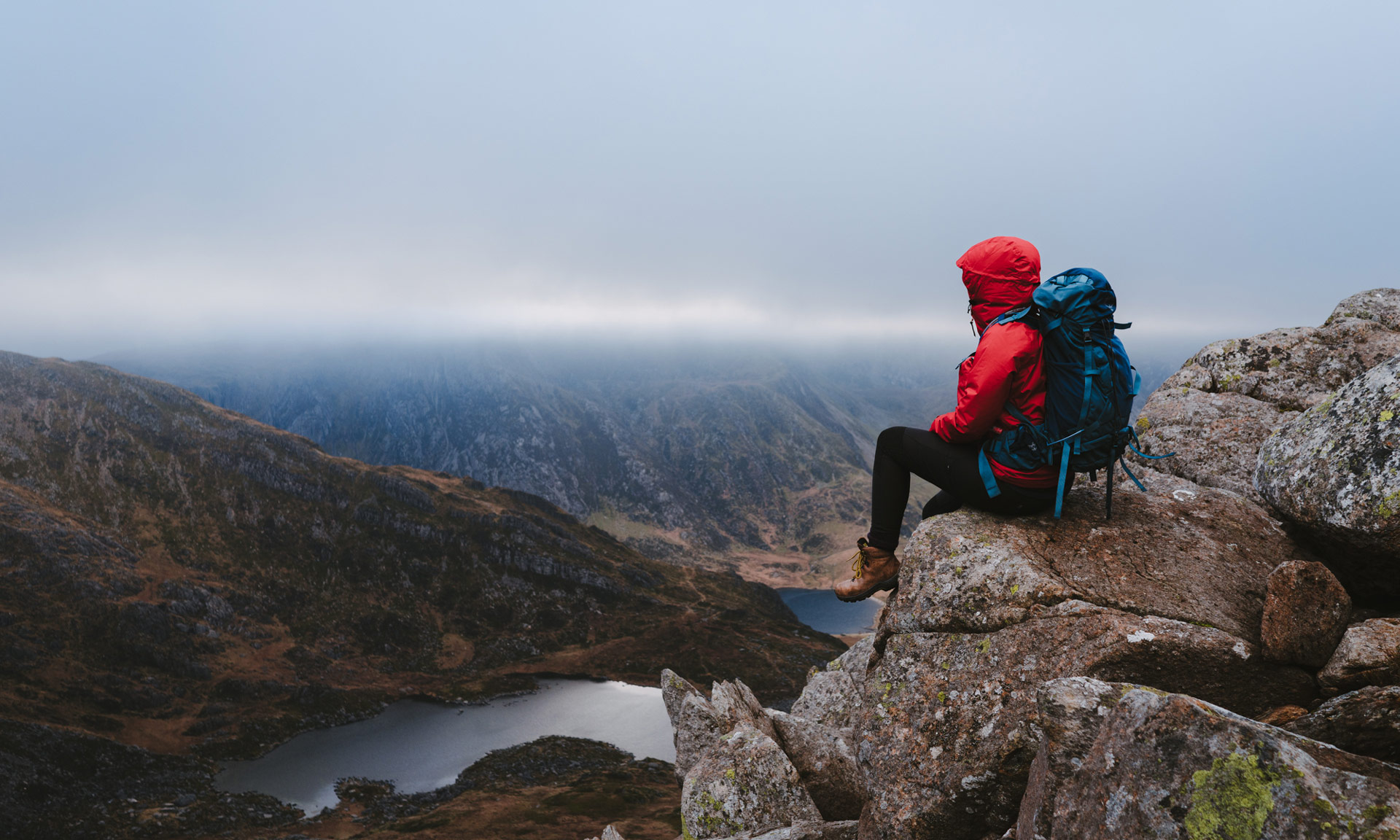 a walker in a red coat sitting on a ledge looking down