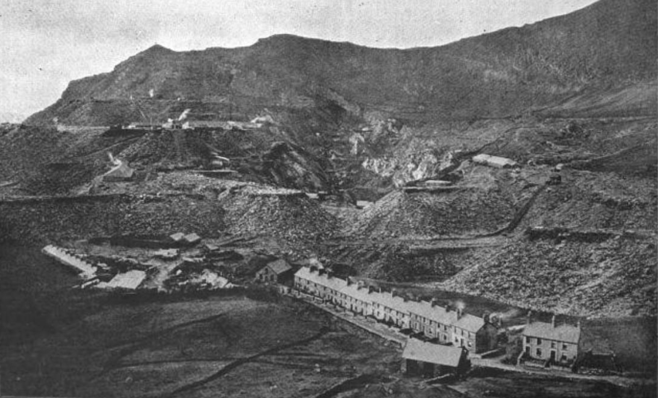 A black and white photo of Oakeley Terrace at Talywaenydd, Blaenau Ffestiniog with a back drop of Oakeley quarry behind.