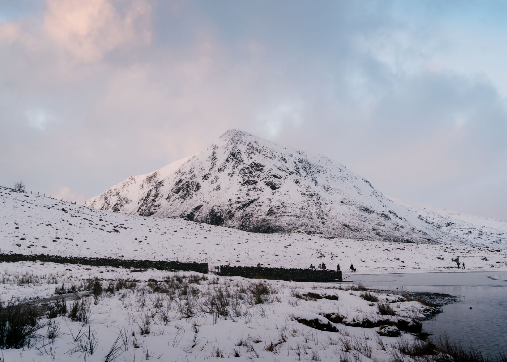 View of walkers on Llyn Idwal lakeside with snow across the landscape