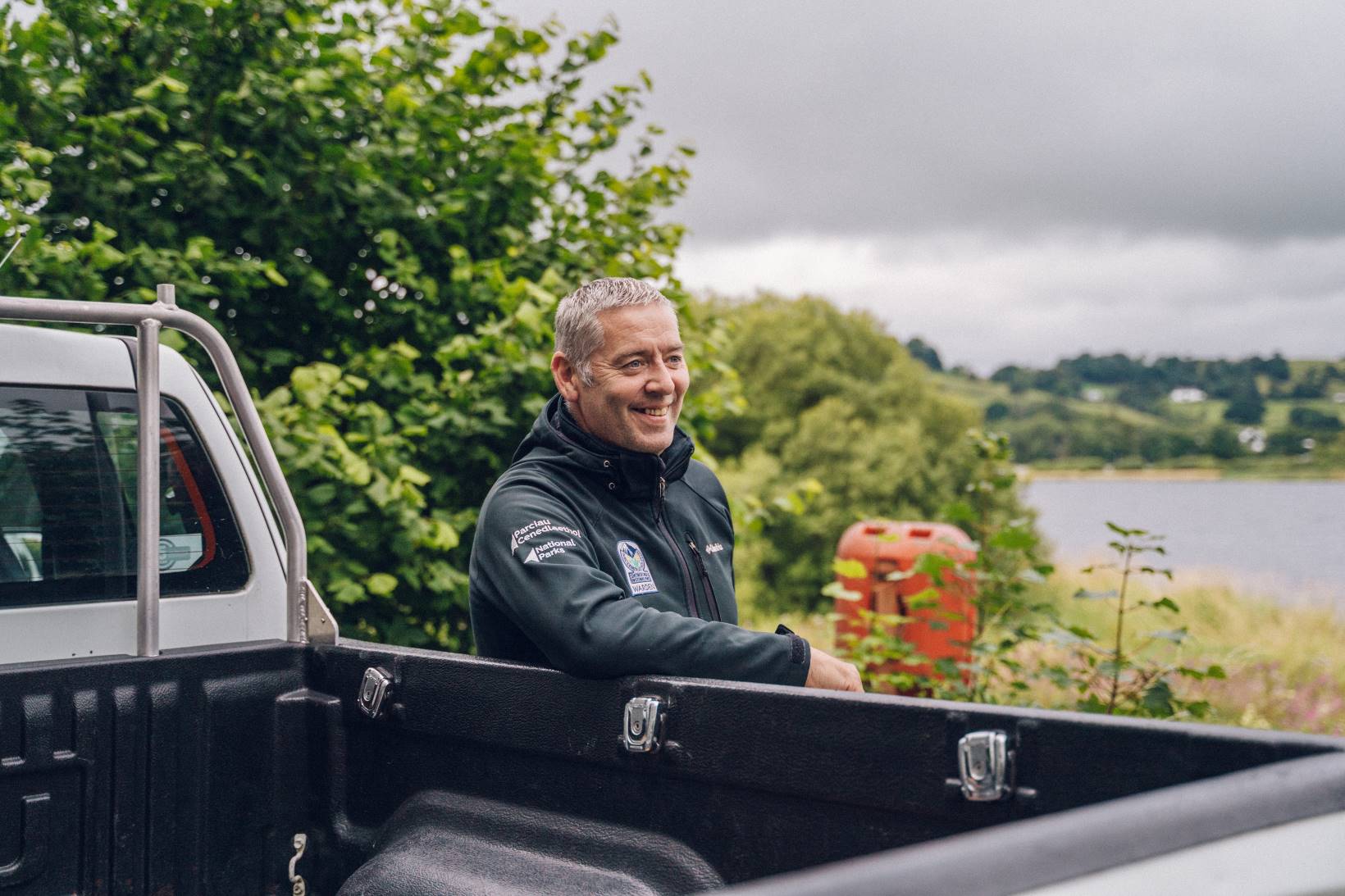 A National Park Authority warden leans on a white pick-up truck.