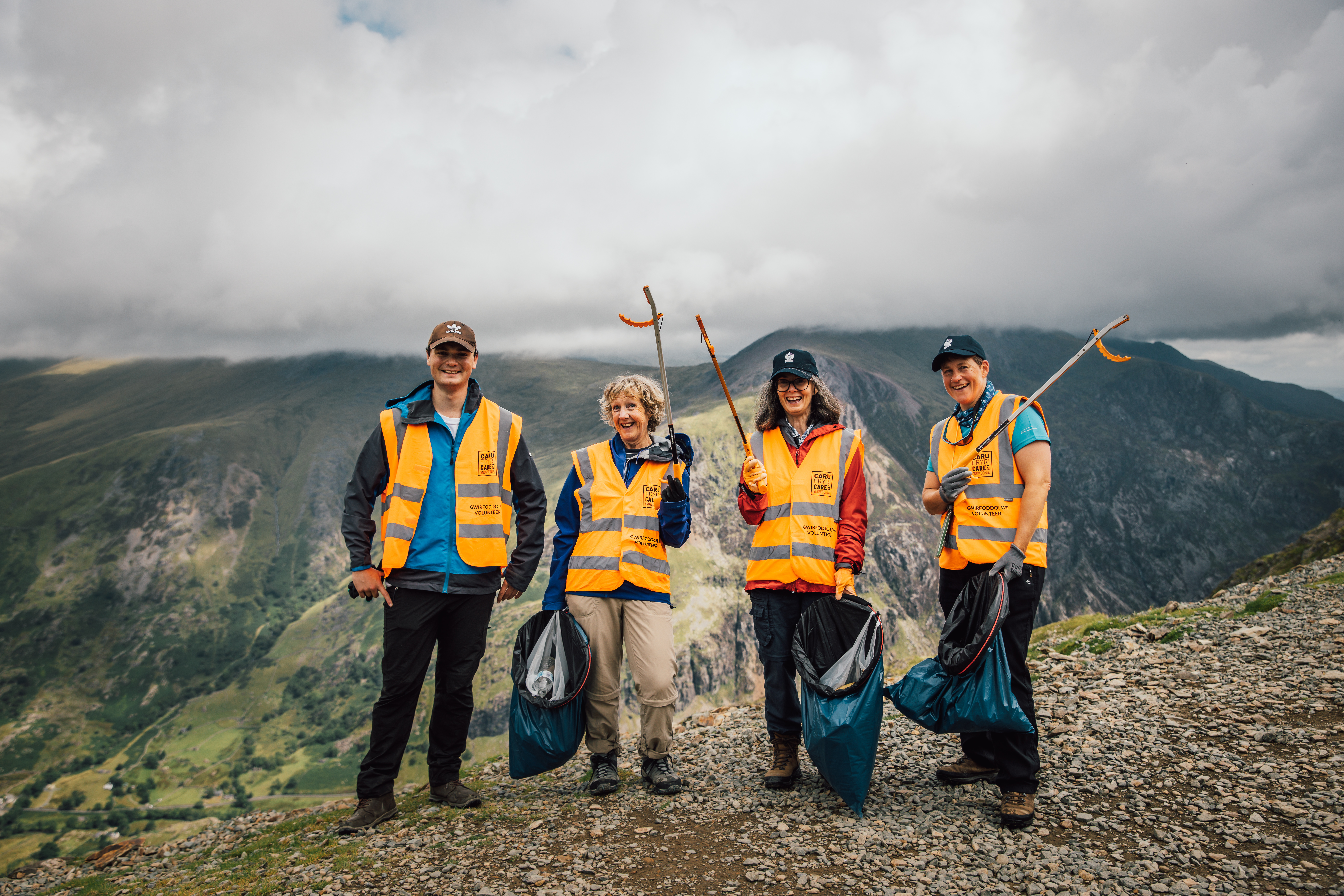 Individuals from Caru Eryri litter picking. They are equipped with litter bags and grabbers, surrounded by a scenic landscape, symbolising their commitment to maintaining the natural beauty of the area.