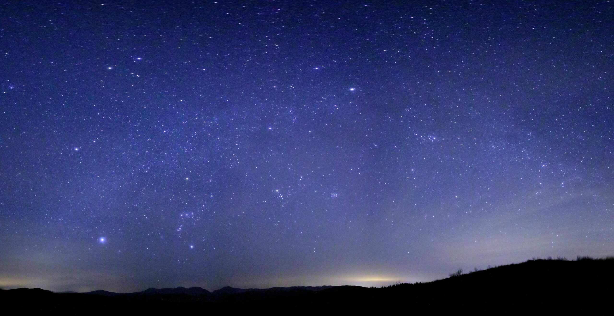 A dark sky filled with numerous stars, including the Milky Way, above a silhouette of mountains.